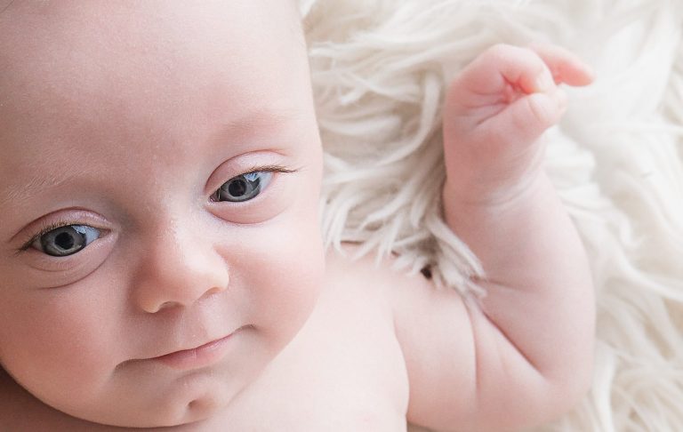Close-up of a smiling baby with blue eyes on a soft white blanket.