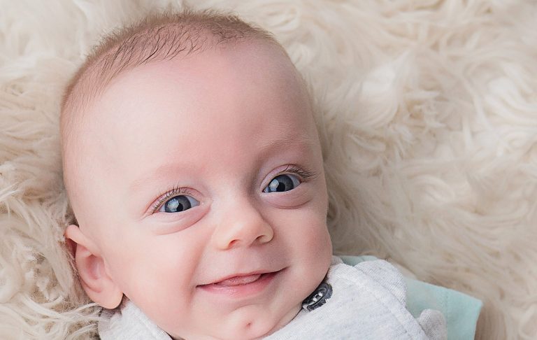 Smiling baby with bright blue eyes, lying on a soft, fluffy surface.