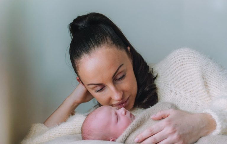 A mother gazes lovingly at her swaddled newborn, both relaxed and content.