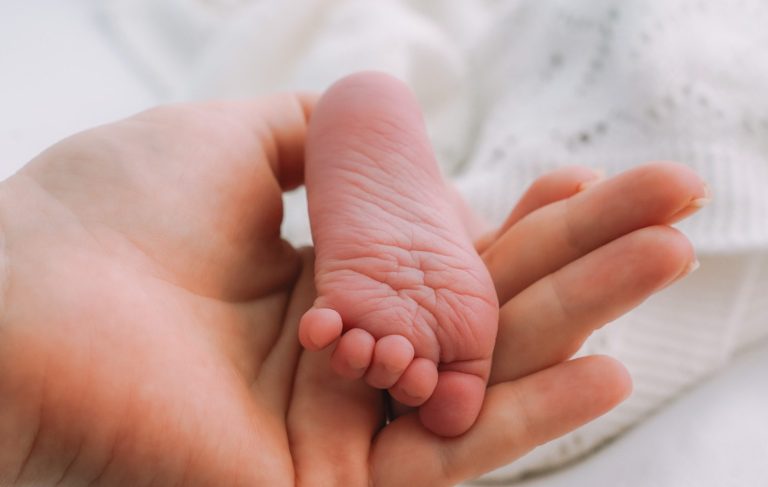 A newborn sleeping peacefully, wrapped in a soft, knitted blanket, held gently in hands.