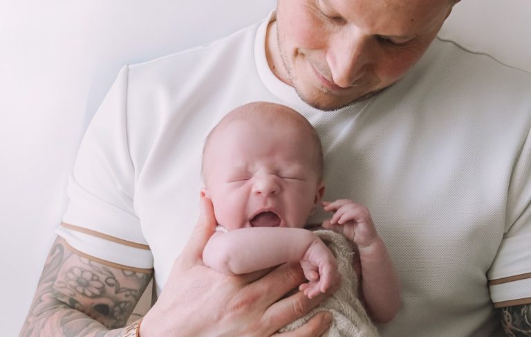 A couple joyfully holds their newborn baby, smiling in a cozy, light-filled setting.
