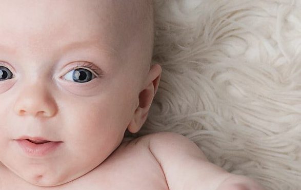 Close-up of a smiling baby with blue eyes on a soft, textured surface.
